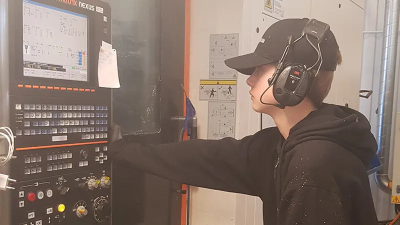 En kille som står och arbetar vid en kontrollpanel i en verkstad.