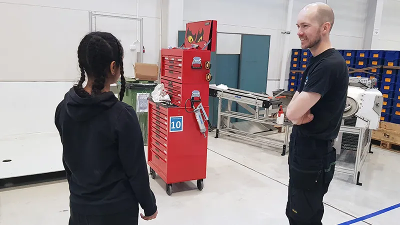 Ungdom i industrimiljö tillsammans med handledare. På bilden syns även verktygsskåp.