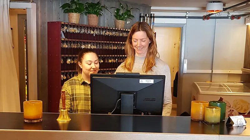 Två kvinnor som står bakom en receptionsdisk och tittar på en datorskärm.